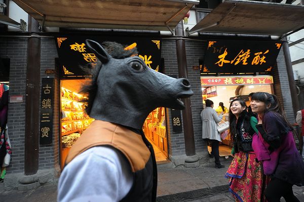 Sourire et bonne humeur au rendez-vous devant un artiste portant une tête de cheval dans les rues de la municipalité de Chongqing, le 10 décembre 2013.