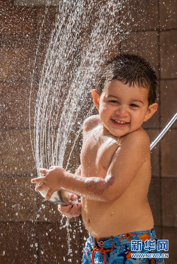 Le 3 juillet à Las Vegas aux Etats-Unis, un petit garçon s'amuse avec l'eau jaillie d'un jet de douche. L'été 2013 a été une saison extrêment chaude dans les régions de l'ouest du pays, dont la températeur n'a cessé de battre des records historiques. (Photo : Xinhua/Zhao Hanrong)