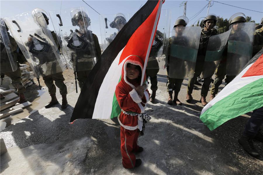 Un enfant palestinien habillé en Père Noël brandit un drapeau palestinien alors qu'il fait face à des soldats israéliens lors d'une manifestation contre la barrière israélienne controversée dans le village de Cisjordanie d'al-Masara, près de Bethléem, le 20 décembre 2013. [Photo / agences]