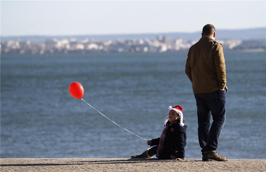 Une jeune fille portant un chapeau de Père Noël joue avec un ballon rouge près du Tage à Lisbonne, le 20 décembre 2013. [Photo / agences]