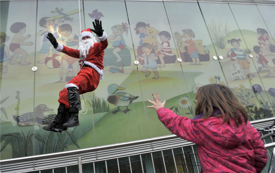 Une fillette salue un membre des forces spéciales de la police vêtu d'un costume de Père Noël, qui descend du toit d'une clinique pédiatrique de Ljubljana, dans le cadre d'un spectacle de Noël pour les patients de la clinique, le 18 décembre 2013. [Photo / agences]
