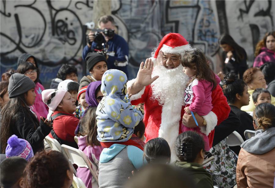 Un homme déguisé en Père Noël accueille les enfants et les familles qui attendent des cadeaux de vacances et des jouets qui seront distribués aux enfants défavorisés à la Mission Fred Jordan à Los Angeles, le 21 décembre, 2013. [Photo / agences]