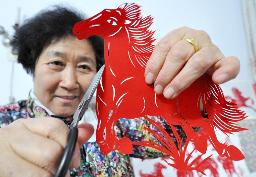 Cai Chun'e âgée de 68 ans, une artiste dans l'art du papier découpé à Handan, la province de Hebei, montre son travail sur le thème du cheval, le 23 décembre 2013. Cai a récemment créé plus de 40 oeuvres dans différentes formes pour mettre en avant tout le charme de ce patrimoine culturel immatériel et souhaiter ses bons voeux pour l'Année du Cheval. [Photo : Hao Qunying/Asianewsphoto]