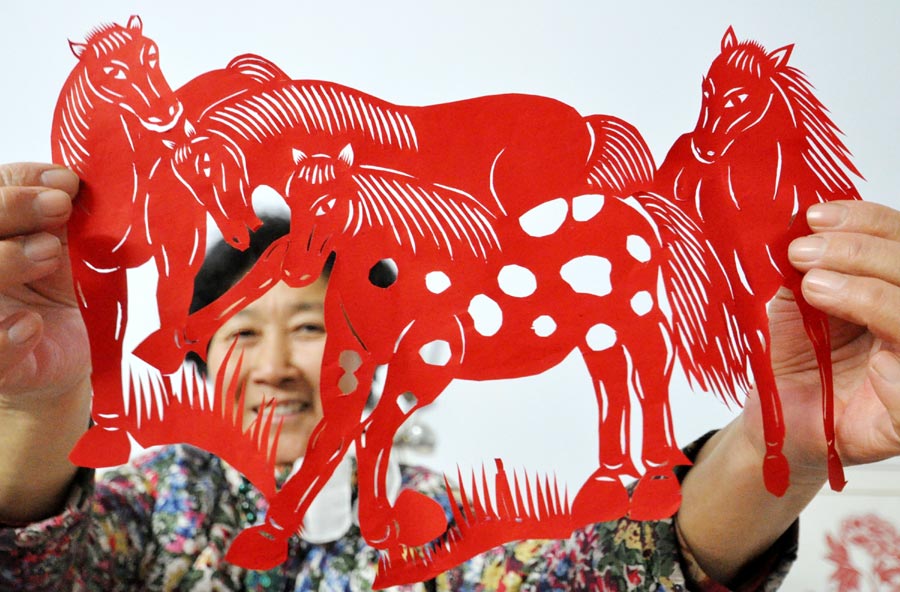 Cai Chun'e âgée de 68 ans, une artiste dans l'art du papier découpé à Handan, la province de Hebei, montre son travail sur le thème du cheval, le 23 décembre 2013. Cai a récemment créé plus de 40 oeuvres dans différentes formes pour mettre en avant tout le charme de ce patrimoine culturel immatériel et souhaiter ses bons voeux pour l'Année du Cheval. [Photo : Hao Qunying/Asianewsphoto]