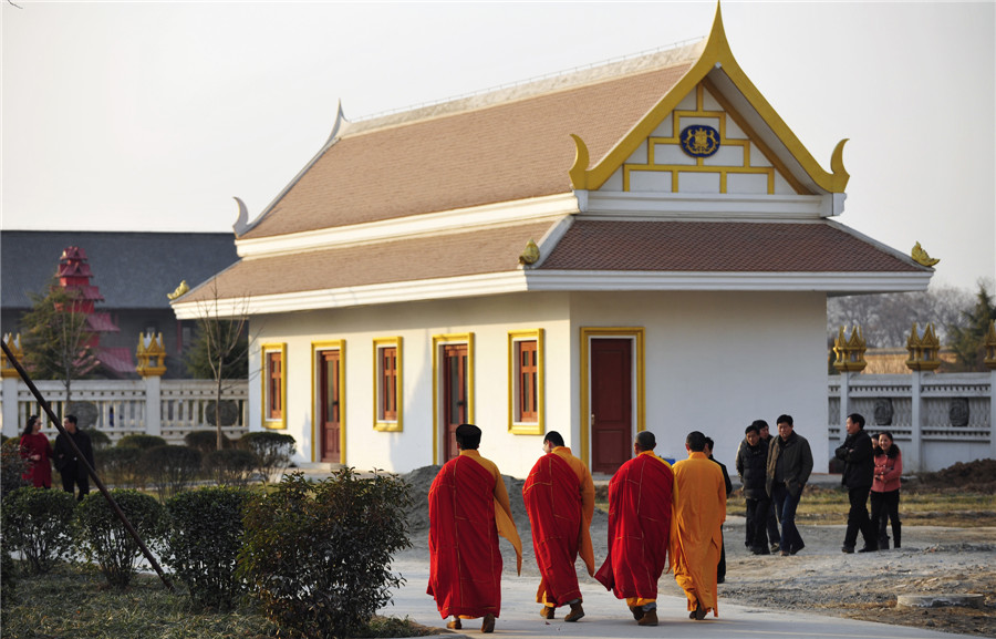 Des moines passent devant une structure bouddhiste de style thaïlandais qui devrait être achevée et ouverte au public dans la première moitié de 2014, au Temple du Cheval blanc, ou Bai Ma Si, dans la ville de Luoyang, dans la province du Henan, au centre de la Chine, le 12 janvier 2014. [Photo / Asianewsphoto ]