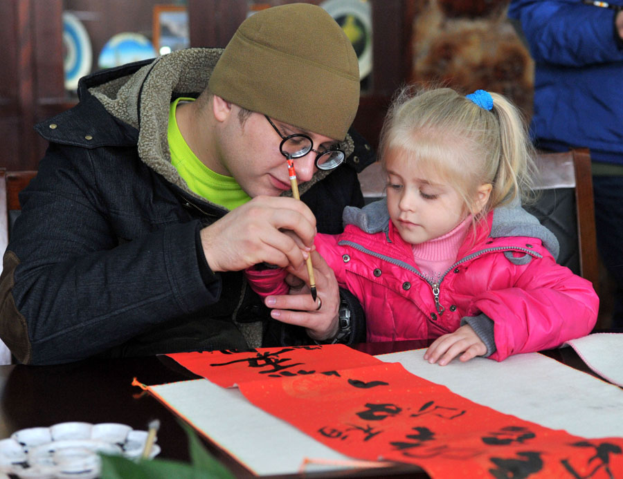 Un étudiant étranger et sa fille occupés à écrire un couplet à Nanjing, la province du Jiangsu en Chine orientale, le 20 janvier 2014. Le couplet, ou quelques vers de poésie écrites sur papier rouge, est une importante décoration pendant la Fête du Printemps, ou le Nouvel An lunaire chinois, étant placé à l'entrée des maisons. Des dizaines d'étudiants étrangers de l'Université de l'Agriculture de Nanjing ont connu la préparation de la prochaine Fête du Printemps, qui tombe cette année le 31 janvier. 