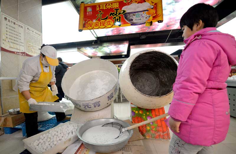 Le 7 février 2014 à Handan, la province chinoise du Hebei (nord du pays), une petite fille observe un employé d'un supermarché confectionner des yuanxiao. Yuanxiao (ou tangyuan), petite boulette de farine de riz glutineux consommée dans une soupe d'eau sucrée, une tradition à l'occasion de la Fête des lanternes, qui tombe le 15e jour du premier mois lunaire chinois, soit le 14 février cette année. Les Chinois préfèrent le plus souvent acheter des yuanxiaos faites à la main. (Photo : Hao Qunying/Asianewsphoto)