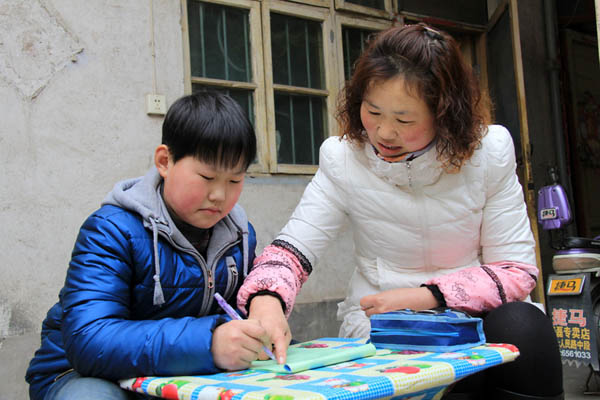 Guo Yangang aide son fils, Li Yuhang, pour la lecture dans le Comté de Wenxian de la ville de Jiaozuo, dans la province centrale du Henan, le 25 février 2014. Mme Guo loue une petite maison près de l'école de son fils, qui lui coûte 5 000 Yuans par an. Pour gagner plus d'argent, elle travaille à temps partiel dans un hôpital, ce qui lui rapporte 1 400 Yuans par mois.