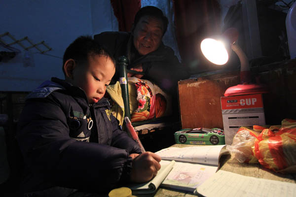 Zhi Chengxiang, 70 ans, aide son petit-fils, Li Xingchen, pour la lecture dans le Comté de Wenxian, dans la ville de Jiaozuo, dans la province centrale du Henan, le 25 février 2014. M. Zhi loue un appartement miteux près de l'école de son petit-fils, qui lui coûte 1 700 Yuans par an. 