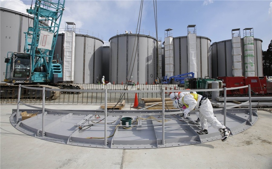 Des hommes portant des combinaisons et des masques de protection travaillent devant des réservoirs de stockage pour l'eau radioactive, en cours de construction dans la zone J1 de la centrale.
