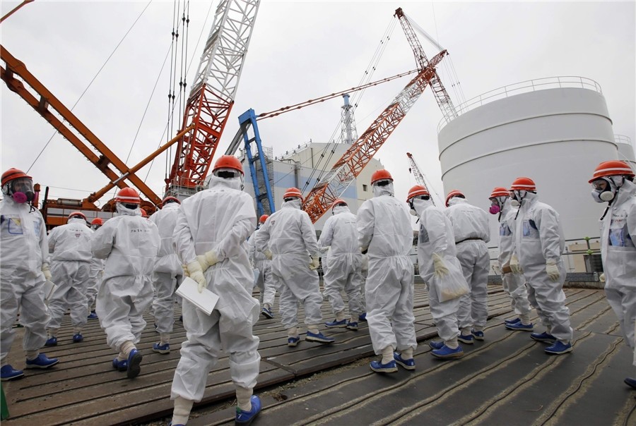 Des représentants des médias et des employés de la Tokyo Electric Power Co. (TEPCO) portant des combinaisons et des masques de protection se dirigent à pied vers le bâtiment du réacteur n° 1 de la centrale.