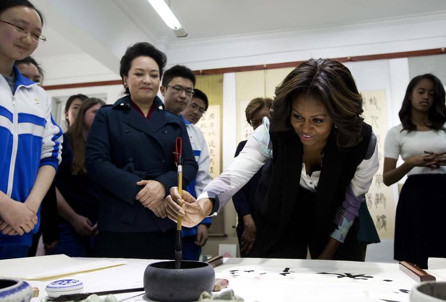 Peng Liyuan (à gauche), l'épouse du président chinois Xi Jinping, montre à la première dame des États-Unis Michelle Obama (au centre) la façon de tenir un pinceau à écrire lors de leur visite d'une classe de calligraphie traditionnelle chinoise à l'École Normale de Beijing, une école qui prépare les étudiants à l'entrée dans les universités étrangères, à Beijing le 21 mars 2014.