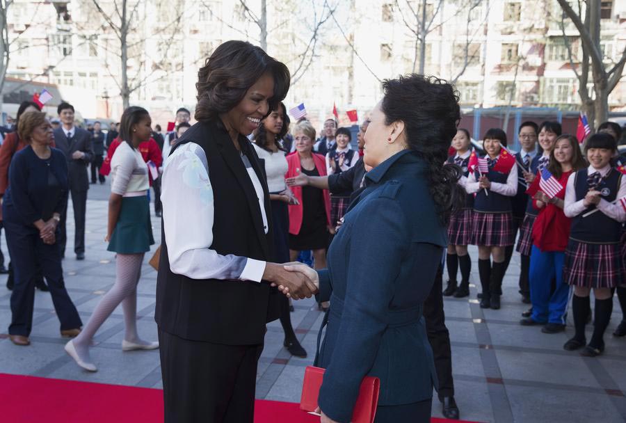 Peng Liyuan (à gauche), l'épouse du président chinois Xi Jinping, montre la première dame des États-Unis Michelle Obama comment tenir le pinceau à écrire lors de leur visite d'une classe traditionnelle de calligraphie chinoise à l'école normale de Beijing, une école qui prépare les étudiants à l'entrée dans les universités étrangères, à Beijing le 21 mars 2014.