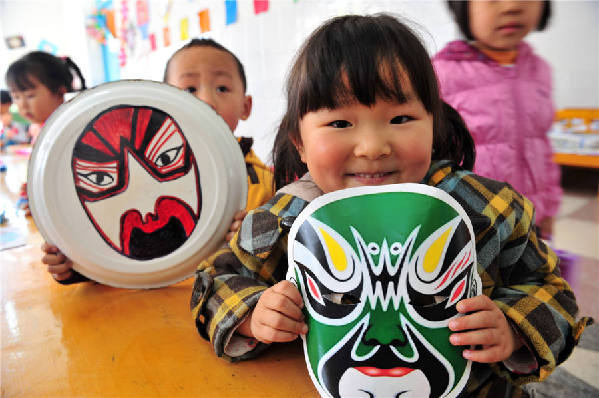 Des enfants montrent leurs masques d'opéra faits à la main dans une école maternelle du Comté de Zigui, dans la Province du Hubei, le 26 mars 2014, pour célébrer la Journée mondiale du théâtre.