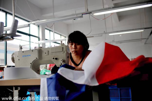 Une ouvrière d'usine coud un drapeau national dans les locaux de la société Hanghzou Donghao Flag Co, dans la province du Zhejiang, en Chine de l'Est, le 8 avril 2014. Le fabricant, qui compte moins de 20 employés, a commencé à recevoir une rafale de commandes pour la Coupe du monde l'an dernier et a produit environ 400 000 drapeaux. Le dernier lot devra être livré au plus tard le 14 avril, deux mois avant la cérémonie d'ouverture. La Province du Zhejiang est depuis longtemps l'un des pôles manufacturiers de la Chine.