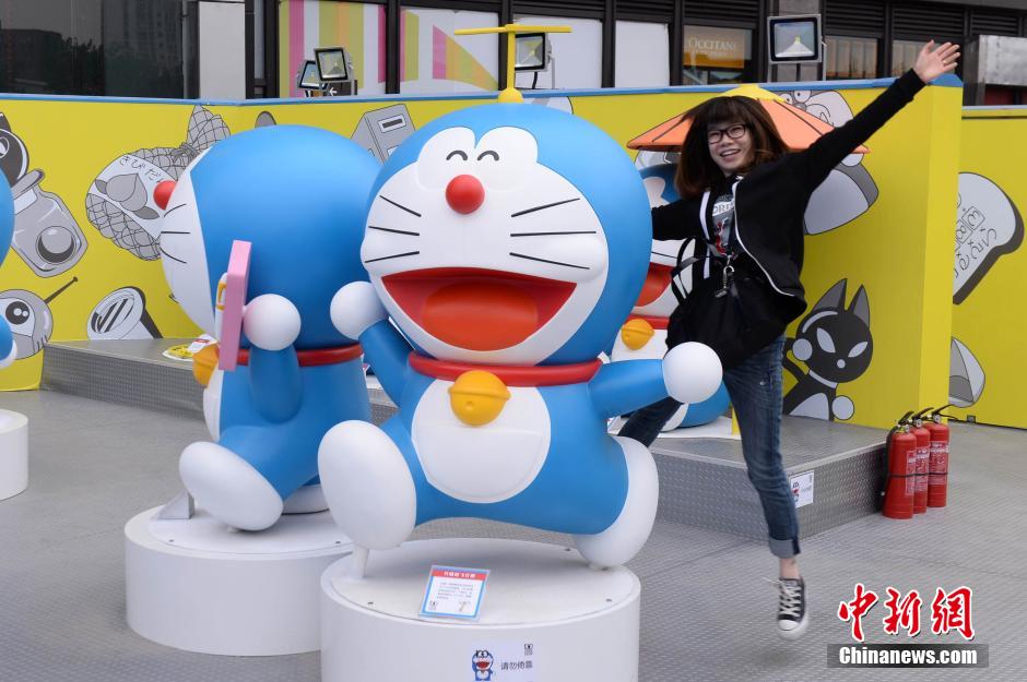 Mercredi 16 avril, devant le centre commercialJoy City du district de Chaoyang à Beijing, une visiteuse prend la pose avec des statues de Doraemon en pré-exposition. (Photo : Chinanews/Yi Ting)