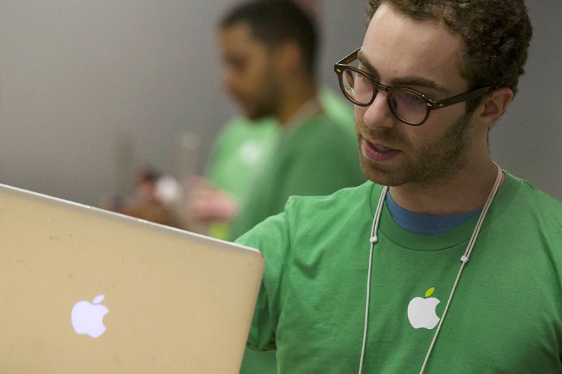 Un Genius de la boutique d'Apple (à droite) aide un client dans la boutique principale de la marque sur la 5e avenue de New York, le 22 avril 2014. Les employés d'Apple portent du vert lors de la Journée de la Terre. [Photo/agences]