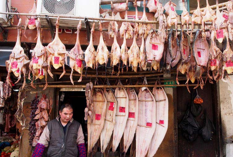 Un vendeur chinois marche sous des morceaux de viande mis à sécher à l'extérieur de son magasin d'alimentation, près de Xintiandi à Shanghai.
